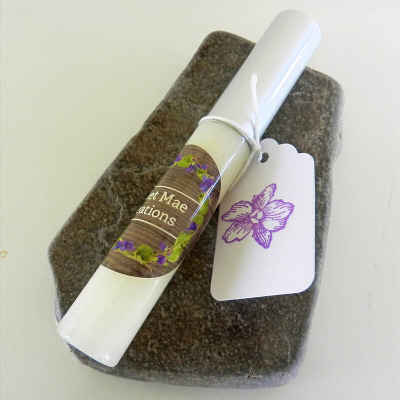 A menthol mint lip gloss tube resting on river stone, tagged with the violet stamp.